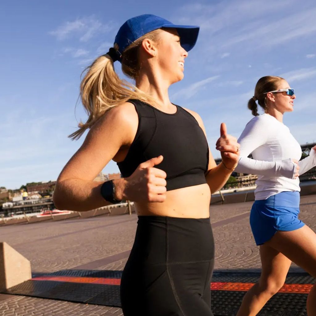 Two women running outdoors in bright morning light, wearing Nimble Activewear sports bras and shorts. Supportive, sweat-ready gear designed for movement and everyday performance.
