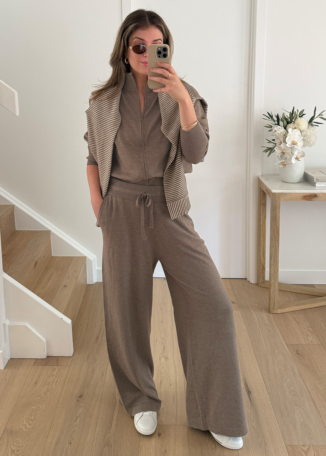 Model taking mirror selfie wearing brown knit lounge set with striped jumper draped over shoulders