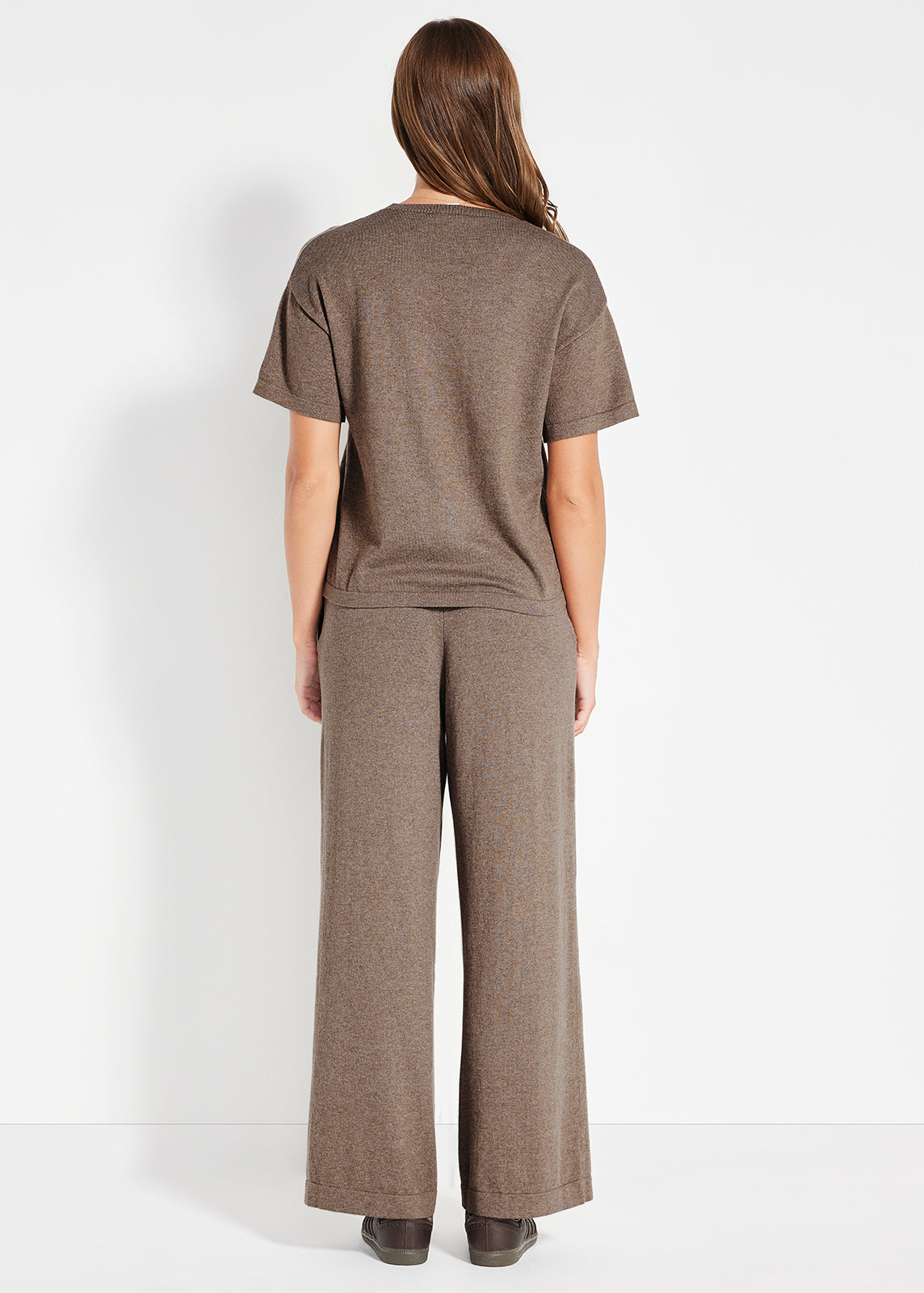 Mirror selfie showing woman in brown knit travel set with striped jumper draped over shoulders and brown tote bag