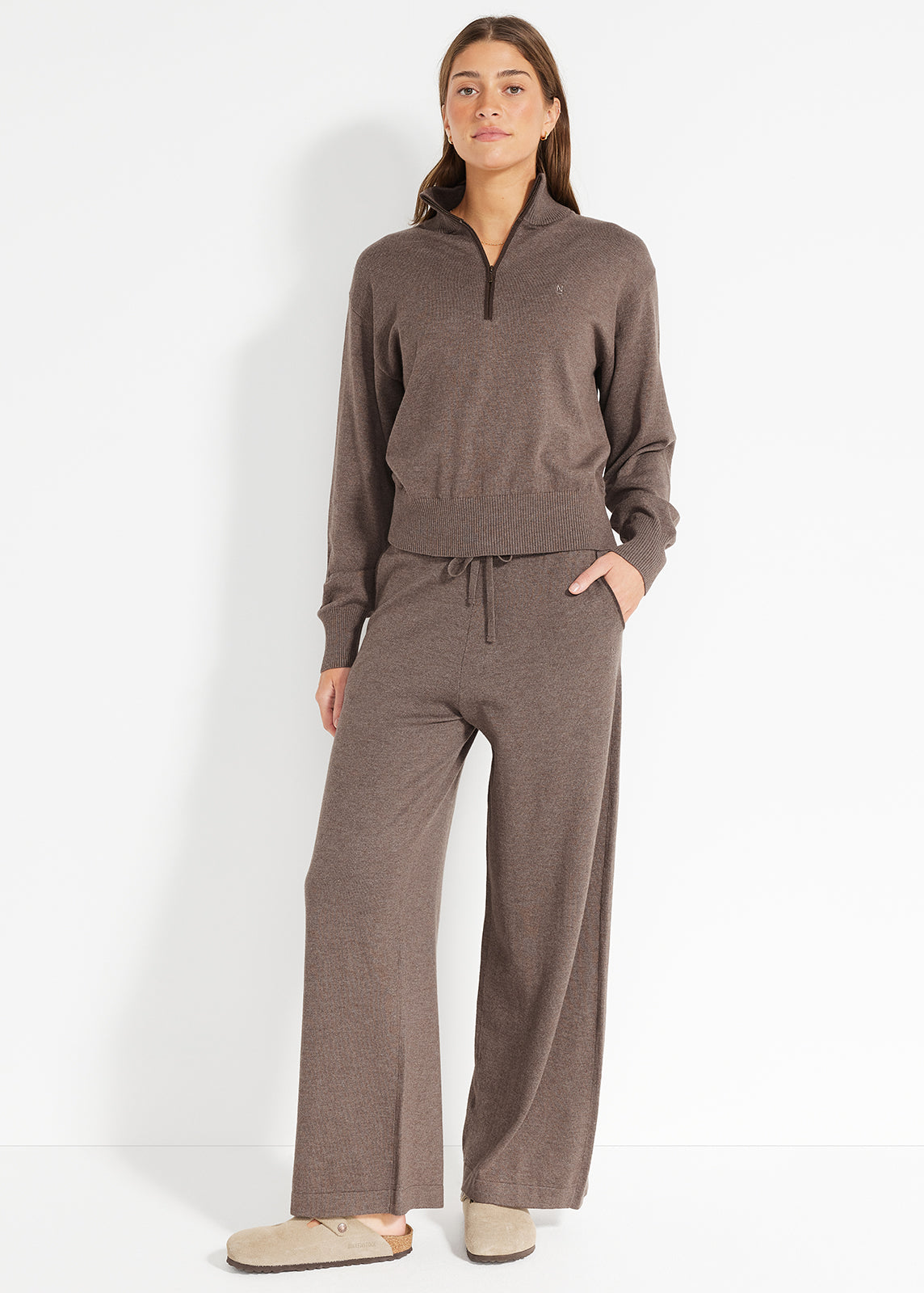 Model wearing brown knit half-zip jumper and matching wide-leg lounge pants with slippers
