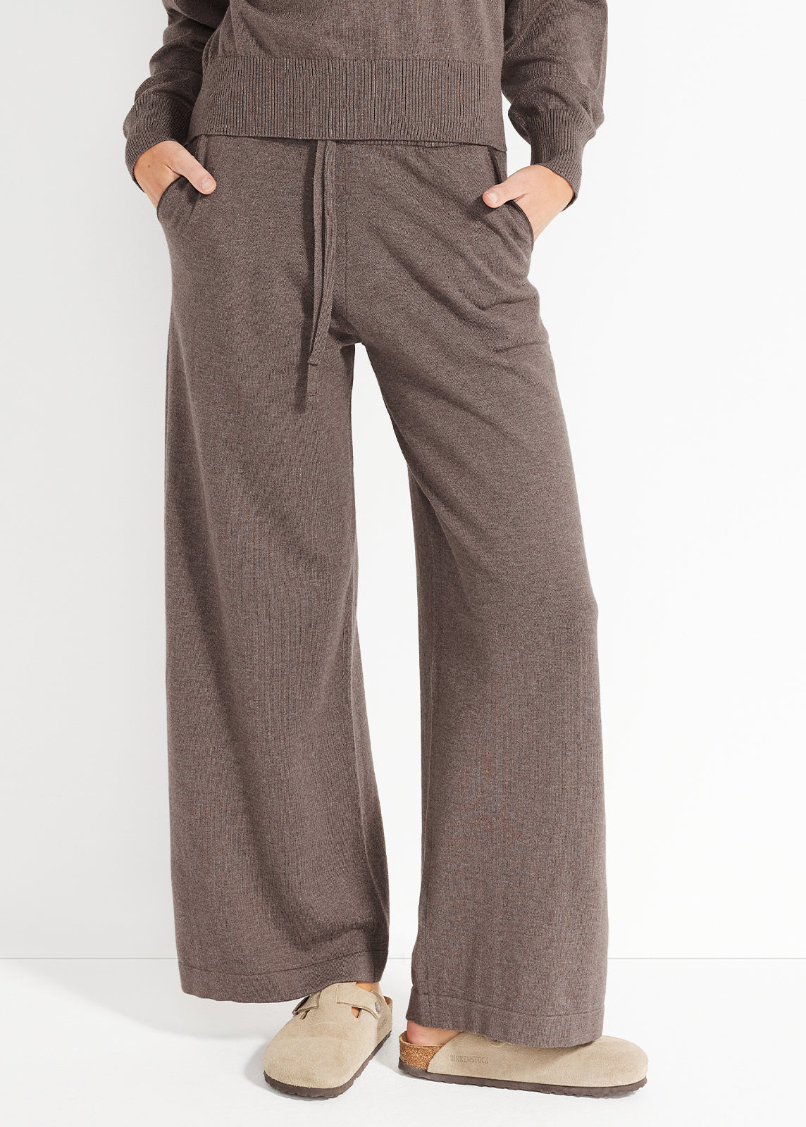 Model wearing brown knit lounge pants with ribbed waistband, drawstring and beige slippers